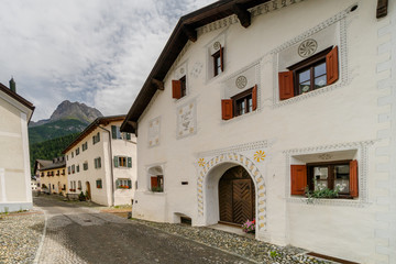 Fototapeta na wymiar cobblestone street lined with typical Engadin houses in the alpine village of Scuol with Piz Lischane in the background