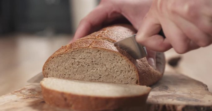 slide shot of young female hands slicing rye wheat rustic bread on cutting board