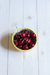 Fresh, sweet cherries in a bowl. White wooden, background.