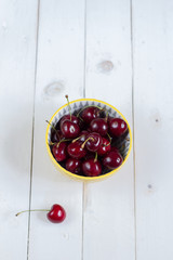 Fresh, sweet cherries in a bowl. White wooden, background.