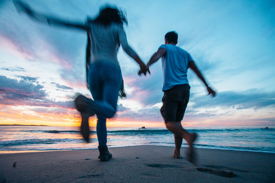 couple holding hands running towards the sea at sunset