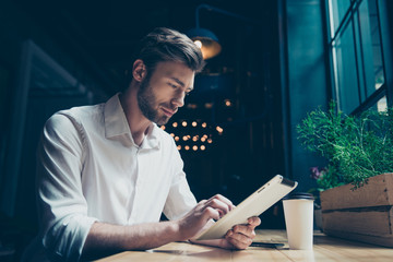 Side view of a young sexy entrepreneur, browsing on his tablet in a dark designed modern cafe, well...