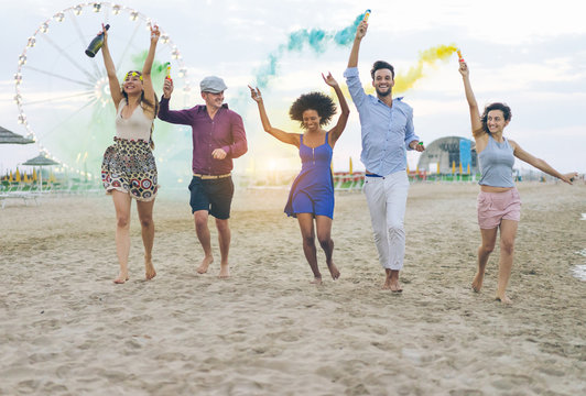 Young friends running with smoke bombs chamagne bottle on the beach at sunse