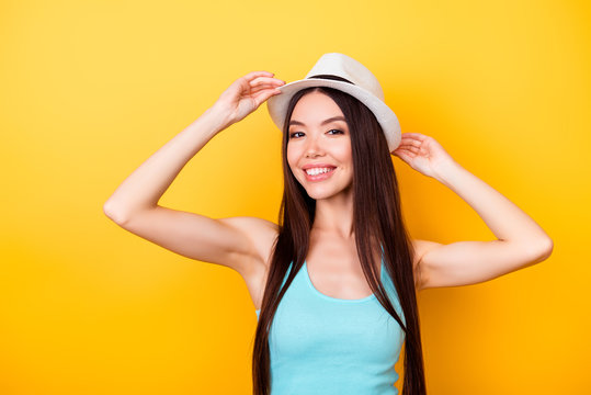 Happy young asian girl on summer vacation. She is in a stylish hat, wearing casual singlet, holding her white cap, amazed, on bright yellow background