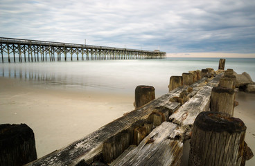 wooden storm jetty and pier leading into a calm Atlantic Ocean under a cloudy sky in the summer in South Carolina