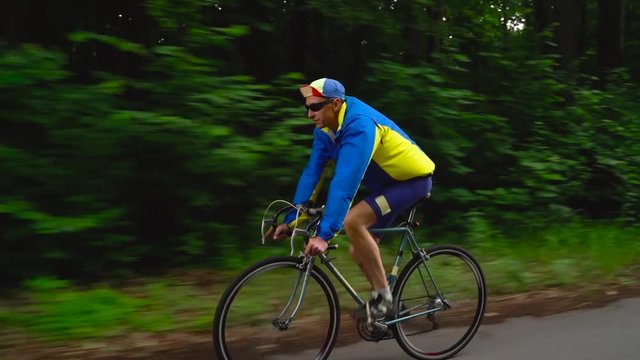 Middle-aged man is riding a road bike along a forest road, slow motion