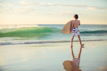 Child having fun with a skim board at the beach at sunset