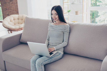 Close up of young happy asian girl typing in her laptop, sitting on beige couch indoors at home, wearing casual outfit