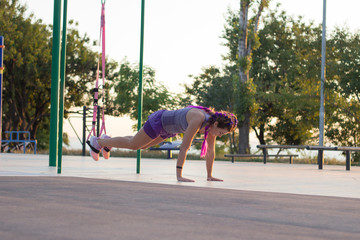 workout with suspension straps In the outdoor gym, fit woman training early in morning on the park, sunrise background  