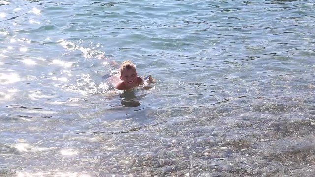 Little kid cheerfully swimming in bright blue seawater. Boy wearing water wings to be safe. Real time full hd video footage.