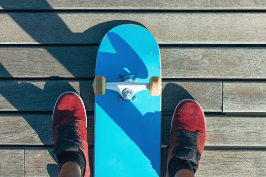 Overhead of blue skateboard on wooden floor. 