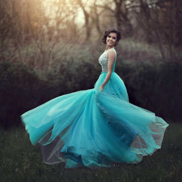 A beautiful graduate girl is spinning in a clearing in a blue dress. Elegant young woman in a beautiful dress in the park. Art photo.