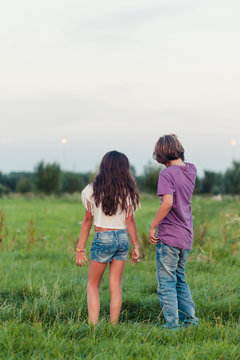 Backside of a boy and a girl standing in a grass field talking to each other 