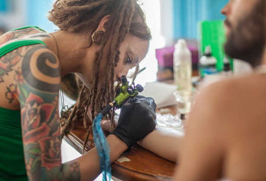 Young Woman With Dreadlocks Tattooing a Client