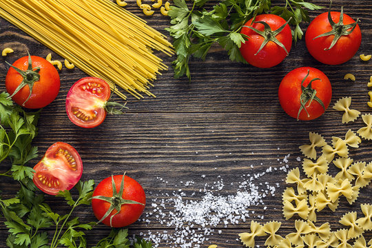 Background with pasta, tomatoes and herb on dark wooden table with copy space.