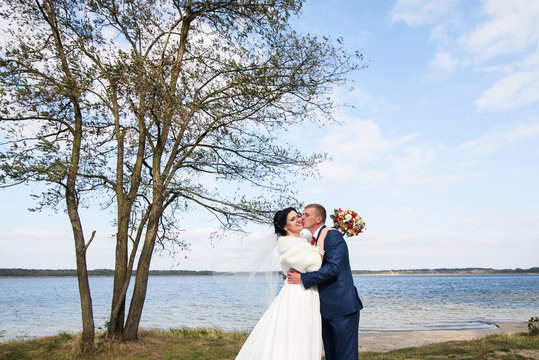 Horizontal photo of a gorgeous newlywed couple posing near the lake