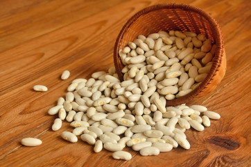 Beans are scattered on a wooden board from a small wicker basket
