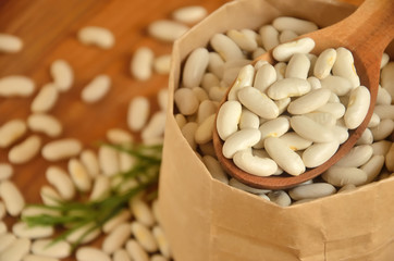 Beans in a paper bag and a wooden spoon with a tarragon stalk