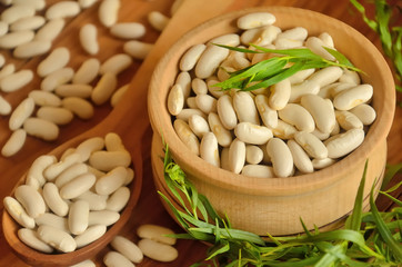 Beans in a wooden bowl and spoon with a tarragon stalks