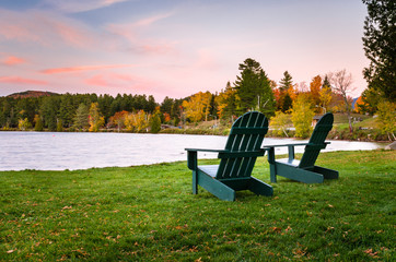 Fototapeta premium Krzesła Adirondack na trawniku Lakeside o zmierzchu. Piękne kolory jesieni.