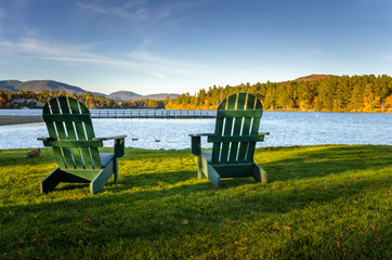 Two Green Adirondack Chairs on the Shore of a  Mountain Lake at Sunset. Lake Placid, NY