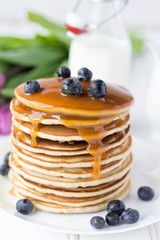 Breakfast Stack of Morning Pancakes with Blueberry and Caramel Syrup  on a Wooden Table  with Purple Tulips and Bottle of Milk