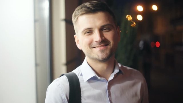 Portrait young male man standing outside smiling nodding nods head agreeing attractive handsome eyes brunette laughing night city lights unfocused street looking camera closeup white shirt agree adult
