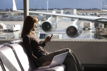 femme en hiver à l'aéroport avec un ordinateur et un téléphone portable et des oreillettes