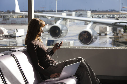 femme en hiver &agrave; l'a&eacute;roport avec un ordinateur et un t&eacute;l&eacute;phone portable et des oreillettes