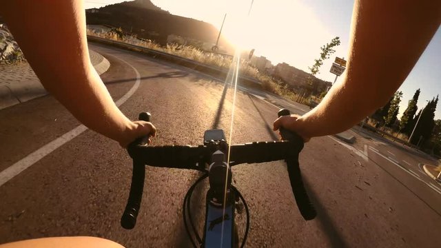POV shot of female road cyclist is riding fast on roundabout at dramatic summer sunset time in the evening.