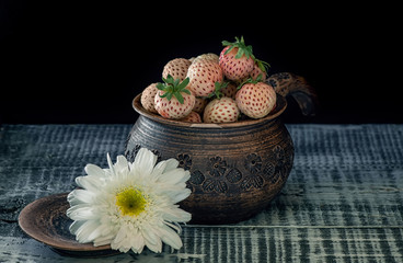 Ripe fresh white strawberries in a clay pot in a rustic style on a black background. Art.