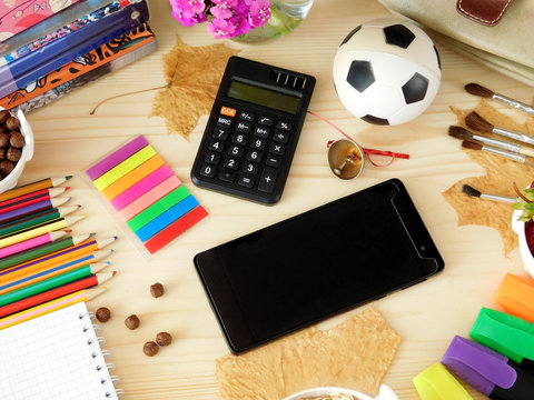 Smartphone with an empty screen and calculator surrounded by school supplies on a wooden background