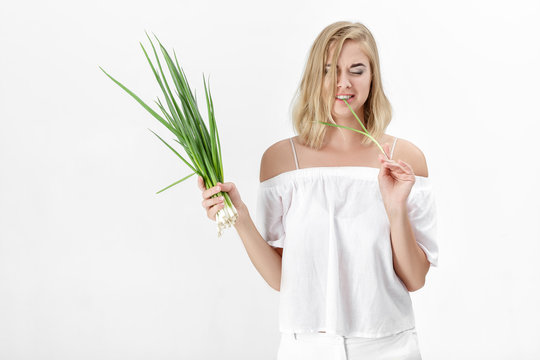 Beautiful blond woman in a white blouse eating green bitter onion on white background. Health and vitamins