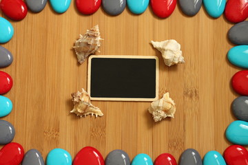 Obraz premium petits galets rouge gris et bleu disposé tout autour d'un plancher de bois de bambou marron avec au centre un petite ardoise vide pour écrire un message