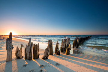 Zonsondergang op het strand van de Oostzee en oude houten golfbreker
