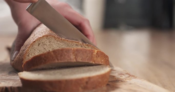 Slow motion slide shot of young female hands slicing rye wheat rustic bread on cutting board