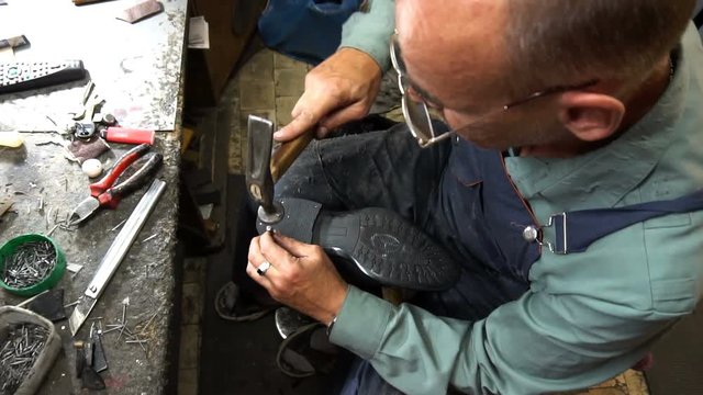 Shoemaker repairing a shoe in workshop 4k. nail the heel cap to the heel