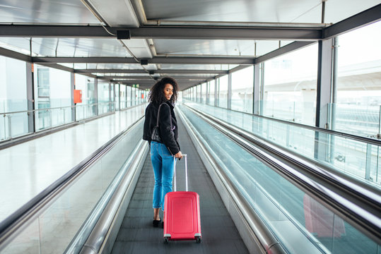 woman in the moving walkway at the airport with a pink suitcase.