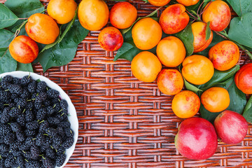 On the wicker table lie orange apricots and a plate with mulberry. 