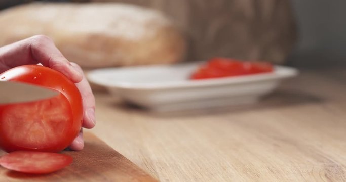 Slow motion slide shot of young man hands slicing tomato on cutting board