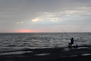Boy fisherman at the sea in the evening