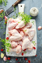 Fresh raw chicken wings on a white cutting board with thyme, chilli, salt, pepper, garlic