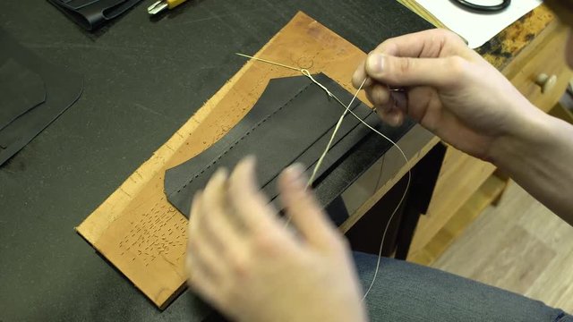 The skinner threads the thread into the needle on the background of the blank for the leather wallet close-up 4k.