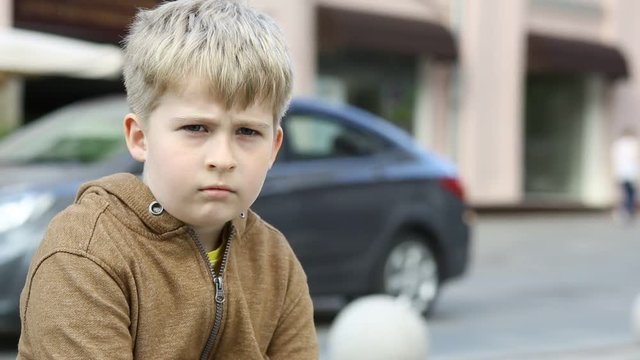 Portrait of a frightened child in the background of moving cars. A sad boy.