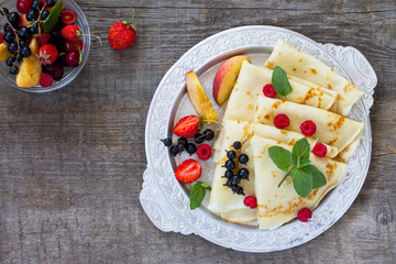 Pancakes with fresh berries of currants, strawberries, nectarines, sweet cherries and raspberries on a wooden kitchen table. Top view, flat lay.