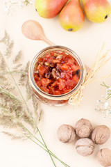 Pear jam with walnuts in a jar on a light yellow pastel background..