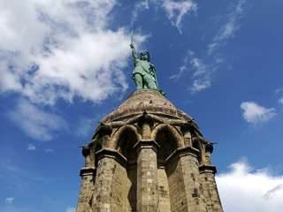 Bizarre weiße Wolken vor blauem Himmel im Sonnenschein über dem Hermannsdenkmal mit Hermann dem...