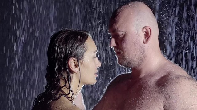naked bald man with hairy body standing naked with his wife in the rain under the light of the moon. the jets of water wash over their hot bodies