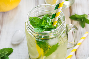 Homemade lemonade. Water with lemon, mint  and ice in glass on a white wooden background. Rustic style.
