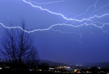 Blue spider lightning cruising over a tree and town lights during a stormy night in France